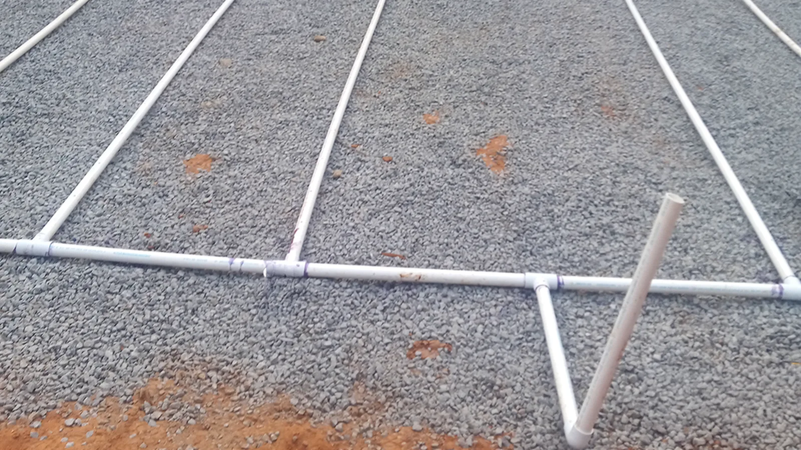 Septic field lines and a connecting pipe laid over a gravel bed during installation.