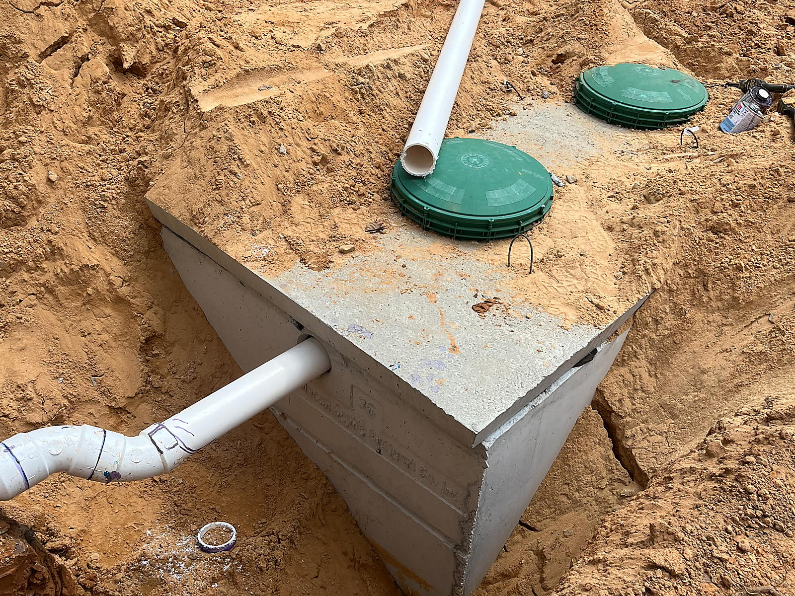 Concrete septic tank with two green access lids and white piping in the Coker excavation
